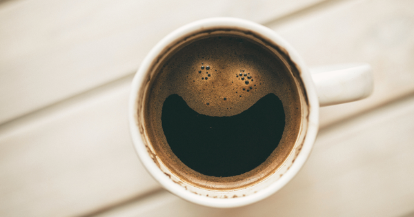 A cup of coffee seen from above, with foam forming a smiling face—proof that humor survives even when nothing else does.